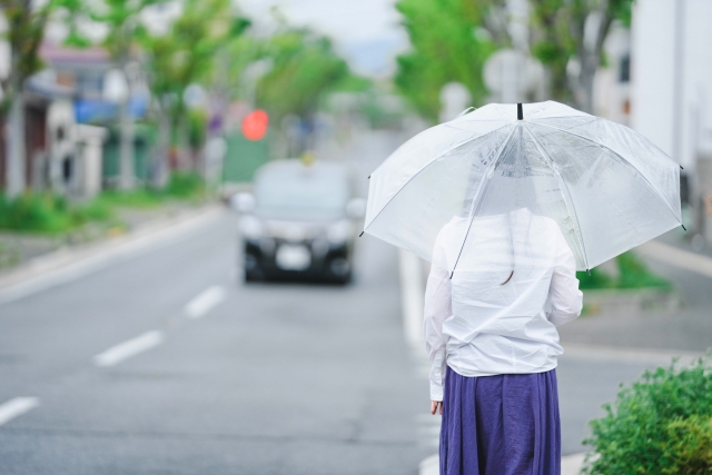 タクシーを探す傘をさす女性