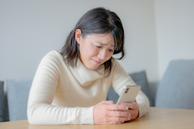 スマホを見つめて悩む女性