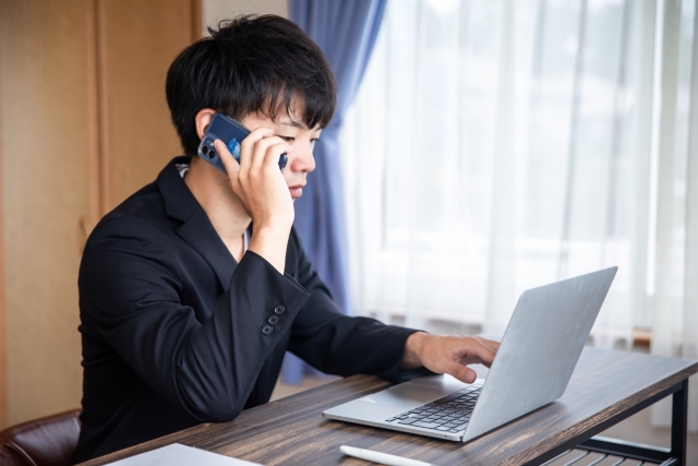 パソコンを見ながら電話する男性